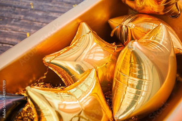 Fototapeta lots of identical gold foil balloons stars in big gold box, festive backdrop, top view, selective focus
