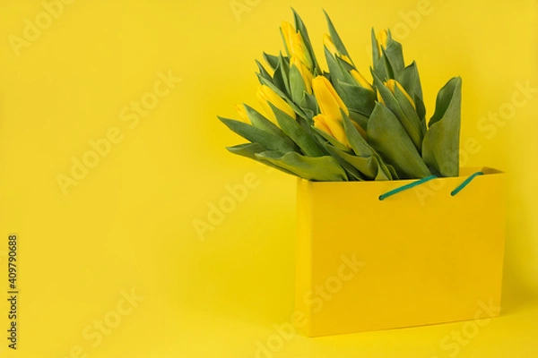 Fototapeta Yellow tulips in a gift bag on a yellow background. Postcard on March 8, Mother's Day, birthday. Flower delivery. Flower Shop. Space for text