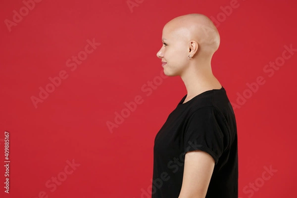 Fototapeta Side profile view of young bald caucasian attractive woman 20s without hair with alopecia problem wearing black basic casual t-shirt looking aside isolated on red color background studio portrait.