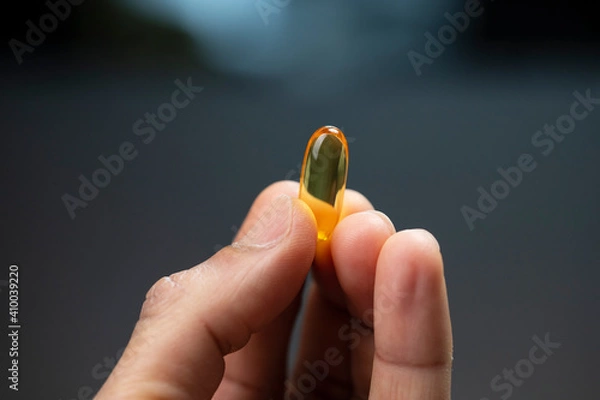 Obraz Close Up View Of A Fish Oil Capsule Between Fingers Of Hand