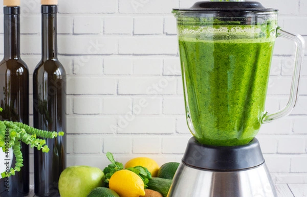 Fototapeta he process of preparing green smoothie in a kitchen blender.  Green smoothie for healthy eating. In front of the white wall