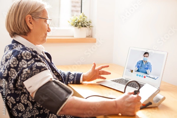 Fototapeta Elderly senior retired woman using sphygmomanometer blood pressure monitor to measure heart rate pulse