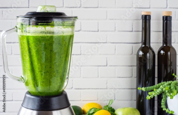 Fototapeta he process of preparing green smoothie in a kitchen blender.  Green smoothie for healthy eating.In front of the white wall