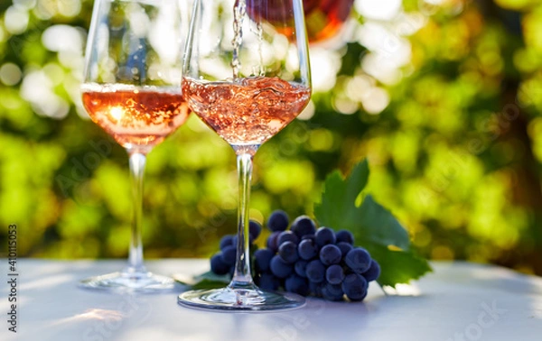 Obraz Pouring rose wine into glasses on a table outside in a vineyard