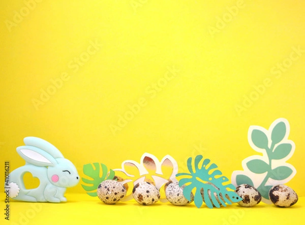 Fototapeta Frame for text with Easter bunny, quail eggs and leaves. Side view on yellow background Easter. Copyspace.