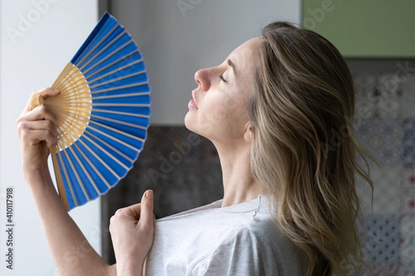 Fototapeta Side view caucasian tired overheated woman in t-shirt using wave fan suffer from heat sweating, cools herself, closed eyes feels sluggish due problem no air conditioner at home at summer weather.
