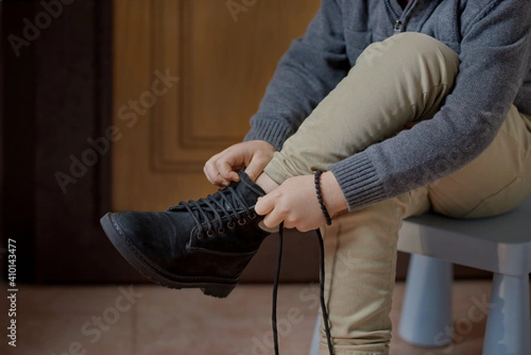 Fototapeta Preschooler child learning to tie shoelaces sitting on the chair at home, selective focus. Step by step instruction. Step 1 