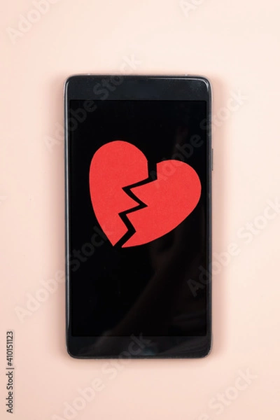 Fototapeta Smartphone with broken red paper heart on it. Parting, unrequited love concept,