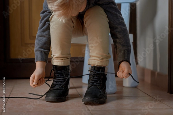 Fototapeta Preschooler child learning to tying shoelace sitting on the chair at home, selective focus. Step by step instruction. Step 3 