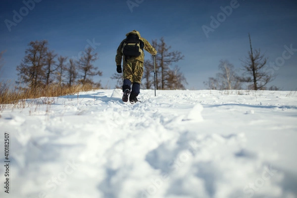 Fototapeta Extreme traveller with a backpack climbs on top of a snow-covered hill in frosty sunny day.