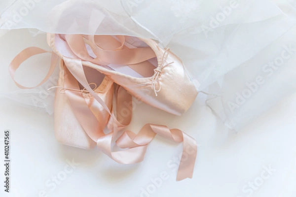 Fototapeta New pastel beige ballet shoes with satin ribbon and tutut skirt isolated on white background. Ballerina classical pointe shoes for dance training. Ballet school concept. Top view flat lay, copy space