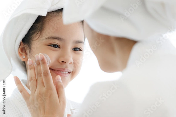 Fototapeta Mother adding treatment cream on the cheek to young and cute Asian girl with spa dress and head covered with a white towel