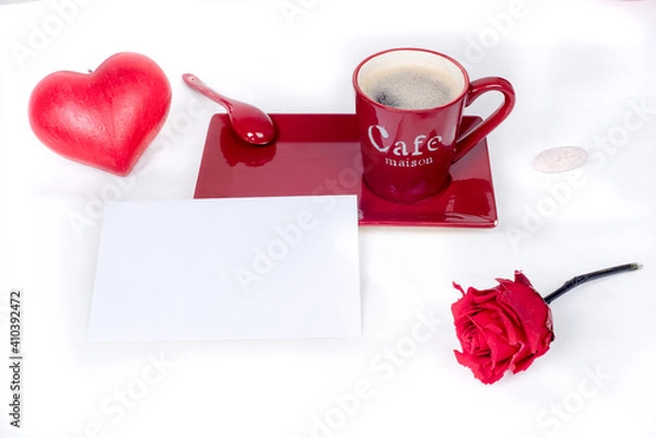Fototapeta Red coffee cup with a white and blank gift card placed in front, surrounded by a red love heart and a red rose., white background. Love and valentine's day 