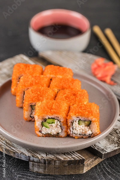 Fototapeta Sushi roll with red caviar and avocado in cream cheese on a dark background close-up.