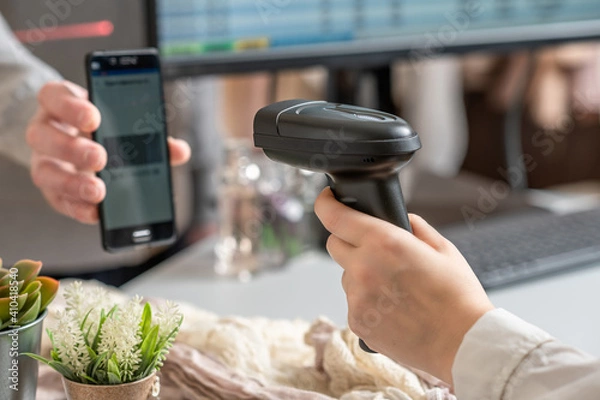 Fototapeta Woman cashier scanning qr code from buyer phone using barcode scanner. Man buying a gift in a female clothing store using promo code.