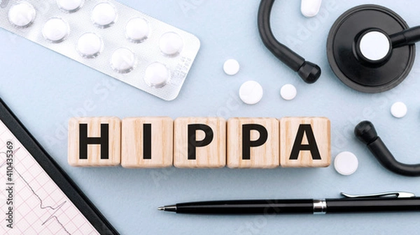 Fototapeta Wooden block form the word HIPAA Health Insurance Portability and Accountability Act on blue background with stethoscope, pills, capsules, pen and cardiogram. Medical concept. Flat lay, top view.