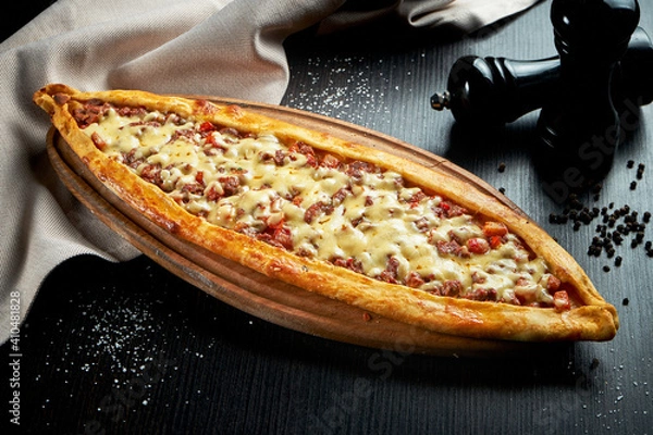 Fototapeta Turkish pide dish with slices of beef, tomatoes and cheddar cheese on black background