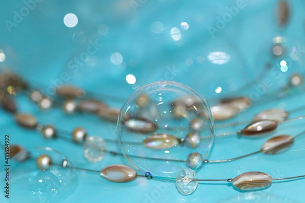 Fototapeta Soap bubbles on a turquoise surface with beads of artificial crystals and opal. Abstract combination of color, soap bubbles and artificial stones