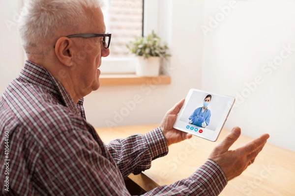 Fototapeta Retired senior elderly man talking to NHS GP female doctor via virtual telemedicine video call using tablet