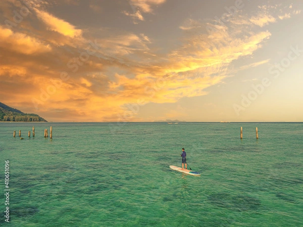 Fototapeta A sunset view with a guy was doing a paddleboard over the beach. 