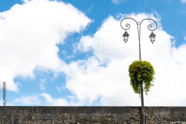 Obraz Very striking lantern with two arches, has placed some colorful flowers. It is on the right side of the image. Blue sky background with clouds.