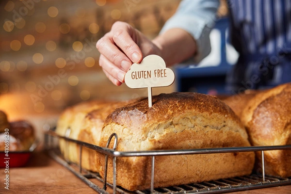 Obraz Sales Assistant In Bakery Putting Gluten Free Label Into Freshly Baked Baked Sourdough Loaves Of Bread