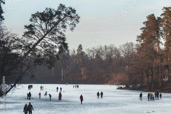 Fototapeta people walking on a frozen lake on a winter evening