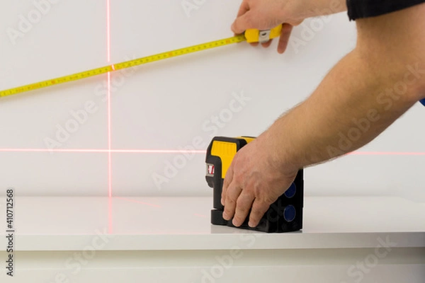 Fototapeta the specialist uses an electronic laser to check right angles and lines while taking measurements of the room