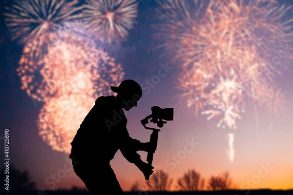 Fototapeta Silhouette of videographer is filming with cinema gimbal video dslr, professional video, videographer in events. Cinema lens on gimbal. Medium shot. Film or cameraman school. Space for text. Fireworks