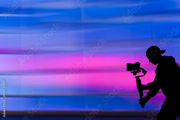 Fototapeta Silhouette of videographer is filming with cinema gimbal video dslr, professional video, videographer in events. Cinema lens on gimbal. Medium shot. Film or cameraman school. Space for text