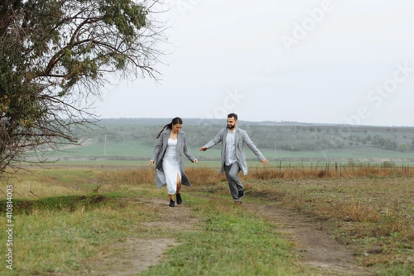 Fototapeta A mischievous couple of newlyweds are running around and having fun in the countryside. Happy moments of the wedding day.