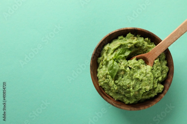 Obraz Bowl of guacamole with spoon on mint background, space for text