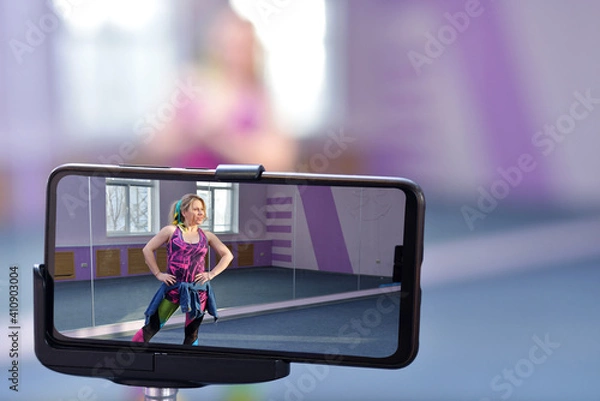 Obraz banner A blonde dancer blogger girl leads online Zumba courses via phone during a pandemic. Online learning concept.