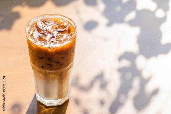 Fototapeta Ice coffee on a wood table with cream being poured into it showing the texture and refreshing look of the drink