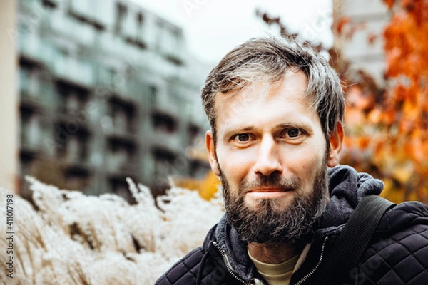 Obraz Smiling handsome young or a middle-aged Caucasian man portraited in the city, with white skin, grey and black hair having a friendly and confident look on his face. Background with fall moody colours 