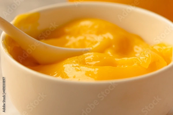Fototapeta Lemon curd in a sausepan white bowl.Close-up yellow smooth background.Horizontal