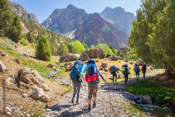 Fototapeta Hikers with backpacks walking in mountains. Group of friends in Fann mountains, Tajikistan. Mountain trail. Tourists hiking.