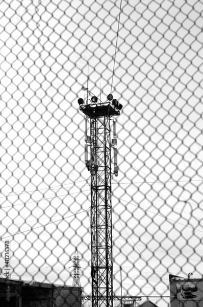 Obraz Lighting tower behind a chain-link fence