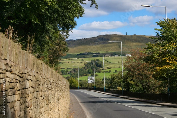 Fototapeta Mossley, England - A view of the rolling hills beside streetlights and an ancient wall on the outskirts of Mossley, under an idyllic blue sky.  Image has copy space.
