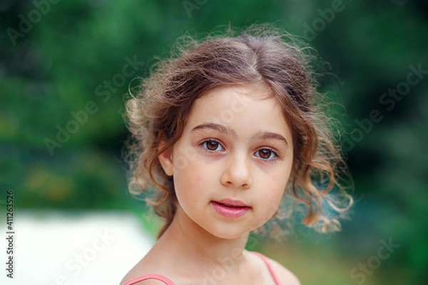 Obraz Portrait of smiling beautiful  little girl at green of summer park. Happy kid looking at the camera