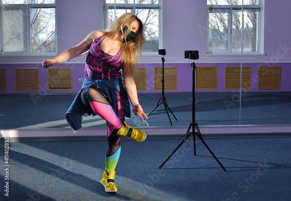Obraz banner A blonde dancer blogger girl leads online Zumba courses via phone during a pandemic. Online learning concept. girl in black mask