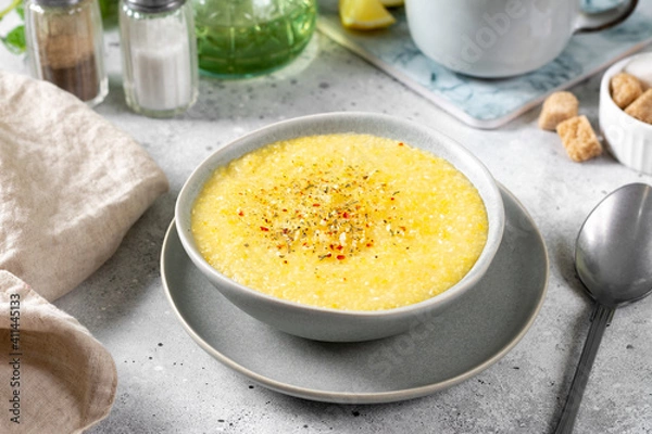 Fototapeta Corn porridge in a ceramic plate on the light gray kitchen table. Porridge of polenta with spices. Cream soup of polenta. Healthy Vegetarian breakfast