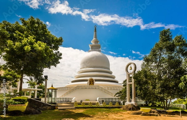 Fototapeta A religious building in Sri Lanka against the background of leafy trees and a blue sky with white clouds