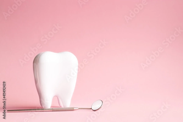 Fototapeta White tooth with dental mirror on pink background in honor of international dentist day with place for text