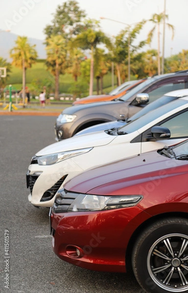 Fototapeta Closeup of front side of red car with other cars parking in outdoor parking area in twilight evening. Vertical view.
