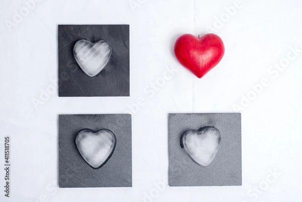 Fototapeta One red love heart, and 3 hearts made of ice placed on 3 slate plates, on a white background. Graphic and geometric, concept of love