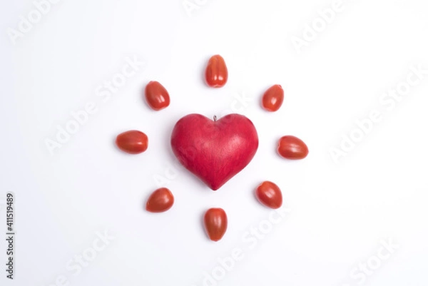 Fototapeta Top view on a red love heart, surrounded by small tomatoes and looking like a shining sun or a flower, white background. Concept of love and valentine's day