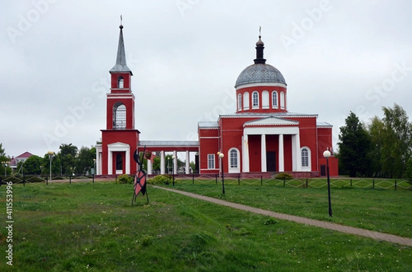 Fototapeta Orthodox church in dark red on a green field against the background of the forest
