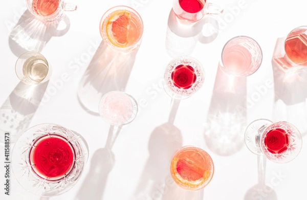 Fototapeta Glasses of colorful drinks with sunlit shadows on bright background. Creative summer party concept.  Flat lay.