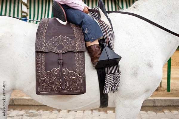 Fototapeta Detail of a little girl riding a horse on a spanish saddle